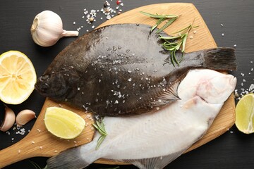 Fresh raw flounder fish and spices on black wooden table, flat lay. Seafood