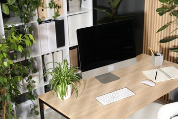 Stylish workplace with modern computer, stationery and floral decor in office. Biophilic interior design