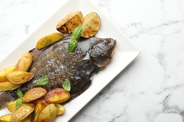 Homemade seafood dish. Tasty roasted flounder fish served with potatoes, basil and lemon slices on white marble table, top view. Space for text