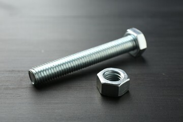 One metal bolt and hex nut on dark wooden table, closeup