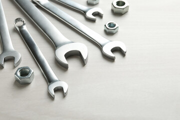 Metal wrenches and nuts on white wooden table, closeup. Space for text