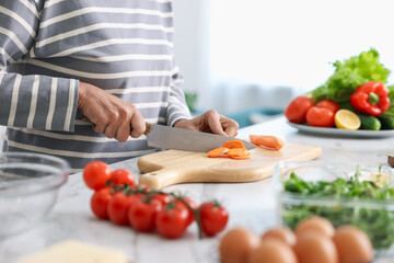 Senior woman cooking at white marble table in kitchen, closeup