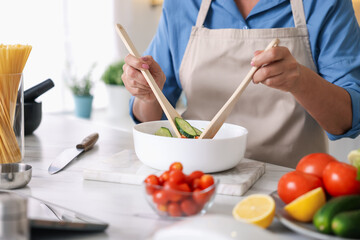 Senior woman cooking salad at white marble table in kitchen, closeup