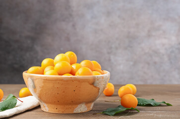 Ripe yellow cherry plums and leaves on wooden table. Space for text