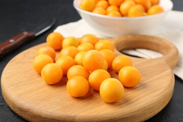 Ripe yellow cherry plums, wooden board and knife on black table, closeup