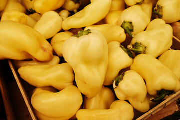 Fresh yellow peppers in a wooden crate at the market. Organic harvest with natural texture, perfect...