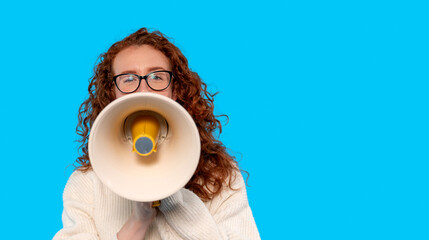 Young woman with curly red hair passionately speaking through a megaphone against a bright blue...