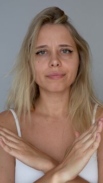 Vertical video of a young blonde woman showing a sign of denial, refusal, rejection crossing her arms in front of her. Girl making a gesture by turning her head left and right, giving negative answer