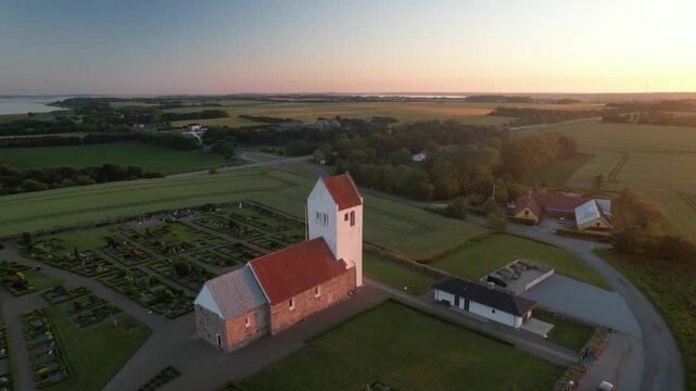 Denmark &ndash; August 23, 2025: Aerial view of a traditional Danish church with a red tile roof surrounded by a cemetery and countryside fields during sunset. Editorial use only.