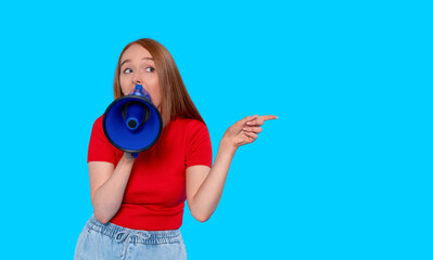 Young woman excitedly shouting through a blue megaphone while pointing to the side against a...