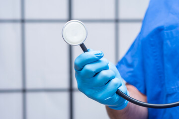 Close-up of a doctor in blue scrubs and protective gloves holding a stethoscope. Concept of...