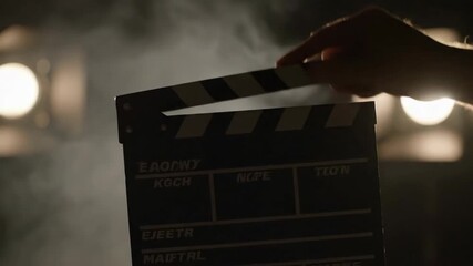 Cinematic Clapperboard in Smoky Setting - A hand holds a film clapperboard against a dark, smoky background illuminated by bright studio lights.