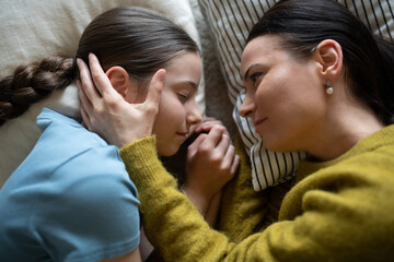 Top view of girl and mom talking in bed, lying face to face.