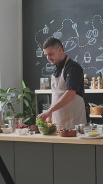 Vertical shot of male food blogger talking to camera explaining recipe while flming cooking vlog at kitchen counter