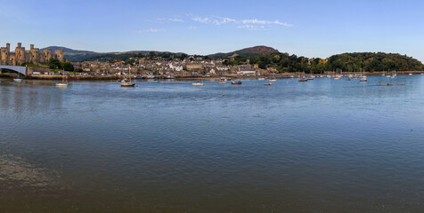 Aerial view of Conwy, Wales, featuring Conwy Castle, the river estuary with moored boats, and the surrounding town under clear summer skies.
