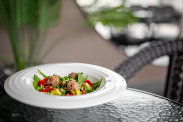 Fresh salad with meatballs, cherry tomatoes, peas, and bell peppers served on a white plate...