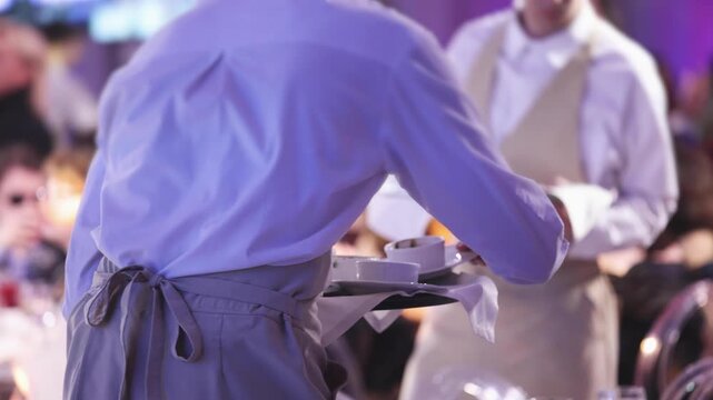 Waiter in uniform serving dishes and drinks on party event dinner, server carrying plates with food and beverages at the table, catering service on wedding reception, table service in cafe restaurant