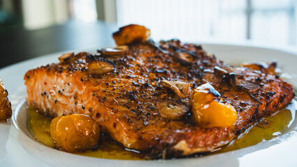 Succulent pan-seared salmon drizzled with olive oil, topped with crispy burnt garlic slices and roasted yellow tomatoes. Gourmet plating, highlighting textures and colors for food branding and culinar