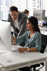 Professional woman sits at desk in modern office, engaging in focused conversation with male...