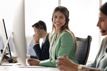 Portrait of Latina female customer support agent or call center representative wear headset sit at...
