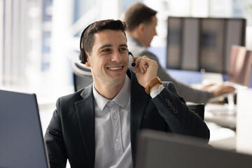 Young Hispanic businessman wearing headset smiling while engaging in call at his workstation in...