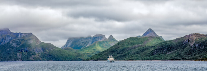 Essential connection across Nordland fjords — a lone ferry moves beneath heavy clouds, where...