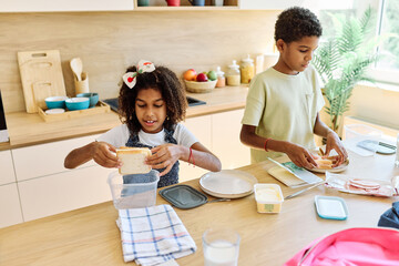 Portret of brother and sister woth school backpacks having fun together preparing sanwiches snack...