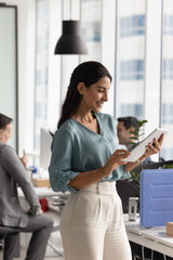 Brazilian professional woman working online using digital tablet standing in contemporary coworking...