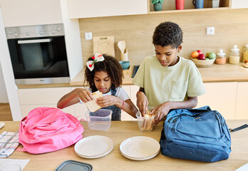 Portret of brother and sister woth school backpacks having fun together preparing sanwiches snack...
