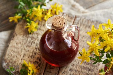 Red  St. John's wort oil in a glass jug with fresh flowers on a table