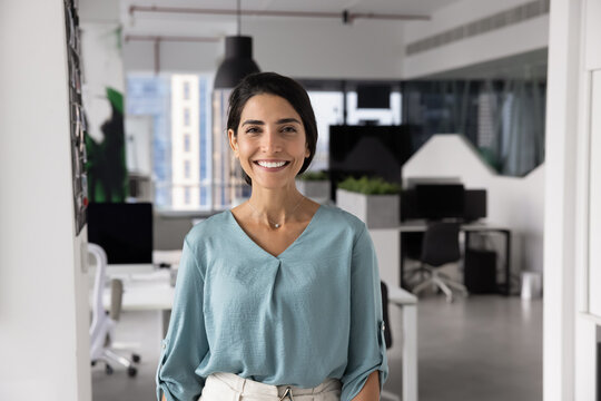 Portrait of young female project manager, marketing specialist or HR consultant dressed in casual attire, stands confidently in modern office, look at camera, radiates friendliness and professionalism