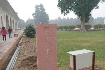 Tourists walking in Agra Fort near a stone sign with directions to different areas of the complex...