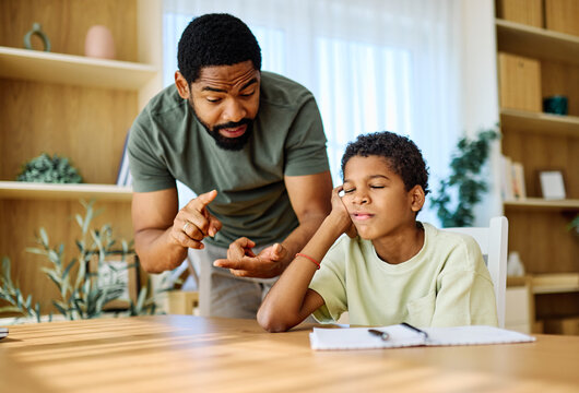 Father and son doing homework fighting and arguing over learning at home. Boy being bored looking through window, Father helping son with homework while showing concern for his frustration - Powered by Adobe