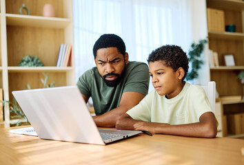 Father and son doing homework with laptop at home. Father and teenage son using laptop. Boy and dad sitting at home working with notebook