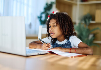 Portrait of a teenage girl having fun using laptop writing and doing homework with laptop at home