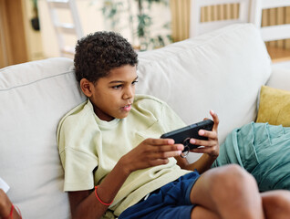Portreit of a black teenage boy having fun using a smartphone mogile phone playing a game or...