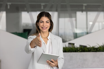 Young 35s Latina businesswoman dressed in elegant jacket extending her hand for handshake, greeting...