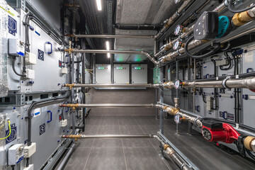 A utility room features numerous pipes and machinery lined along the walls. Mechanical room...