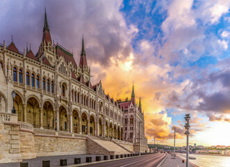 Side view of Hungarian Parliament from Danube embankment at sunset, showcasing neo-Gothic architecture with towers, spires, and central dome against twilight sky. Budapest, Hungary.

