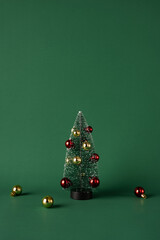 Small vertical decorative Christmas tree adorned with red and gold ornaments, set on a green background. Perfect for holiday greeting cards, festive decorations, or Merry Christmas themed purposes