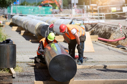 Workers installing pre-insulated district heating pipeline at an urban construction site. Ideal for: energy infrastructure projects, public utility visuals, and civil engineering documentation.