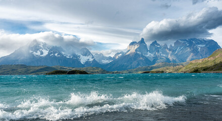 Iconic panoramic view of the turquoise Lago Pehoé and the jagged, snow-capped Cuernos del Paine mountain range on a sunny day in Torres del Paine National Park, Patagonia.