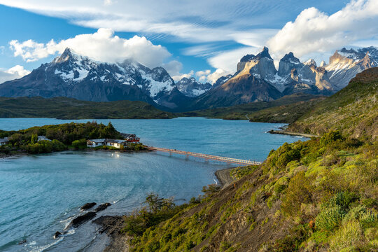 Majestic golden hour light illuminates the iconic Cuernos del Paine mountain range, overlooking the serene Lago Peho&eacute; with its scenic footbridge in Torres del Paine National Park, Patagonia.