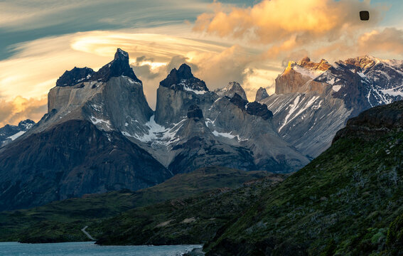 Golden hour light illuminates the iconic Cuernos del Paine peaks under a dramatic, fiery sky with lenticular clouds in Torres del Paine National Park, Patagonia.