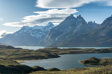 Iconic panoramic view of the turquoise Lago Pehoé and the jagged, snow-capped Cuernos del Paine mountain range on a sunny day in Torres del Paine National Park, Patagonia.