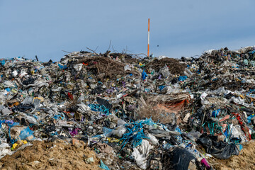 Waste piles collected at a landfill site under a clear blue sky during the day in a suburban area
