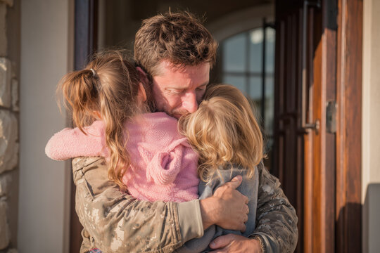 Father embraces daughters in heartfelt reunion at home after deployment in military service during afternoon sunlight