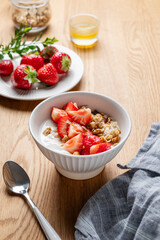 Granola or muesli with natural greek yogurt, strawberry and honey in a bowl on a wooden background