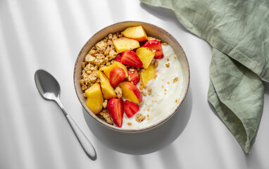 Granola or muesli with natural greek yogurt, strawberry and peach in a bowl on a white table near...