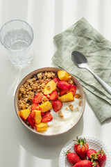 Granola or muesli with natural greek yogurt, strawberry and peach in a bowl on a white background